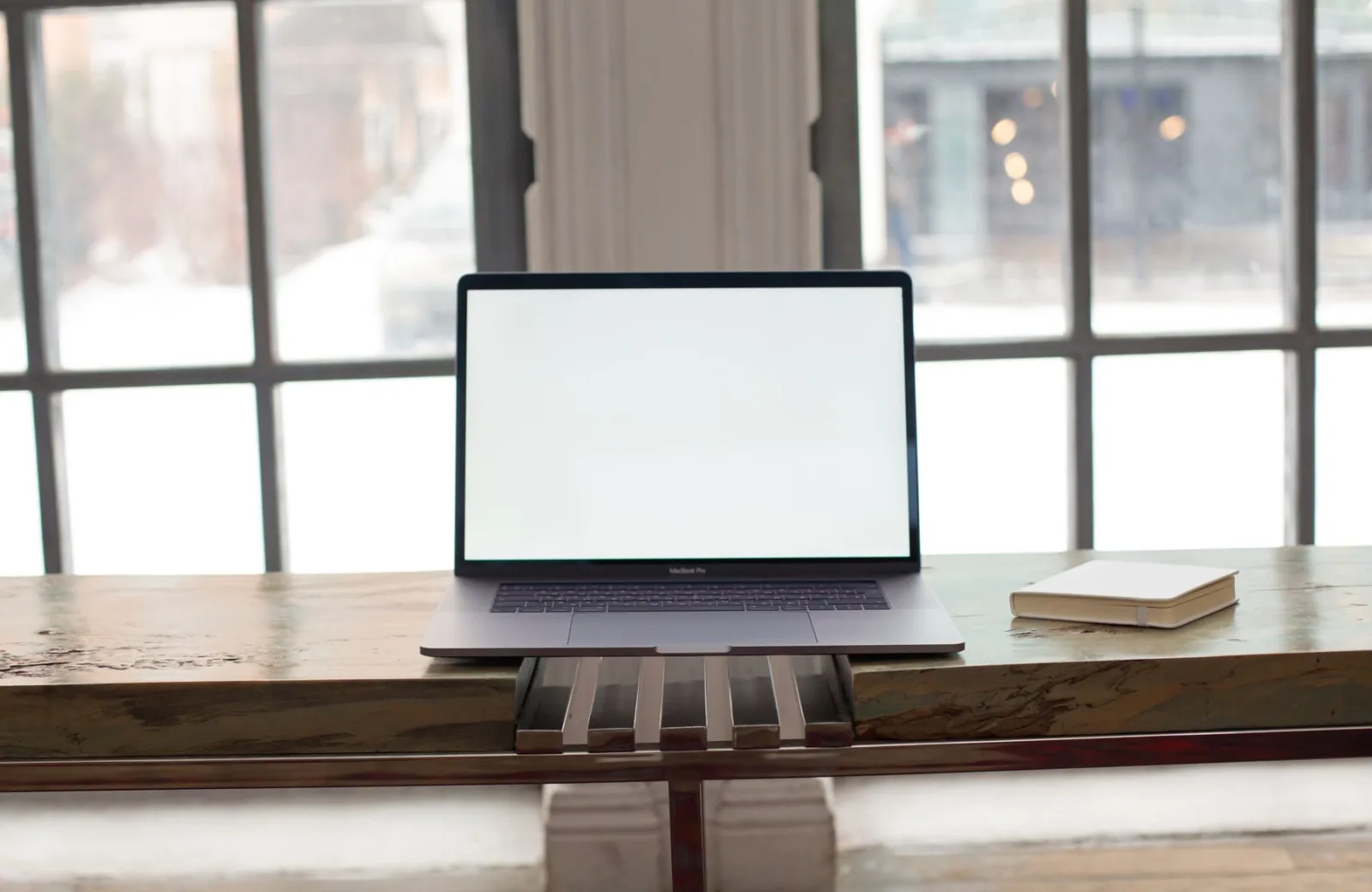 A laptop open on a desk in front of tall windows.