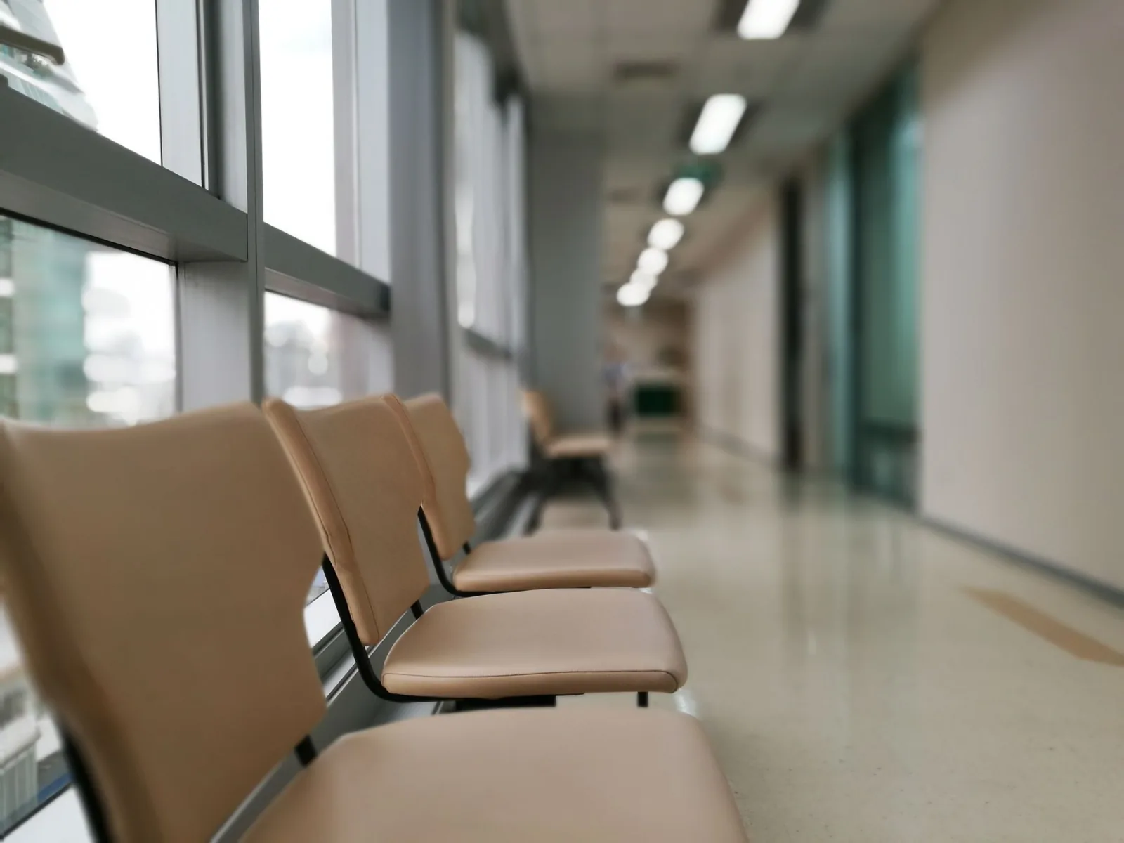 A row of empty waiting room chairs beside a window.